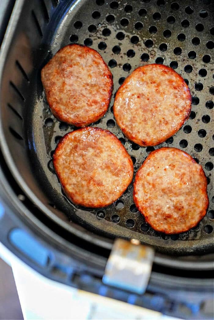 Four cooked sausage patties in an air fryer basket, showing just how easy it is to make delicious sausage patties in air fryer for a quick breakfast.