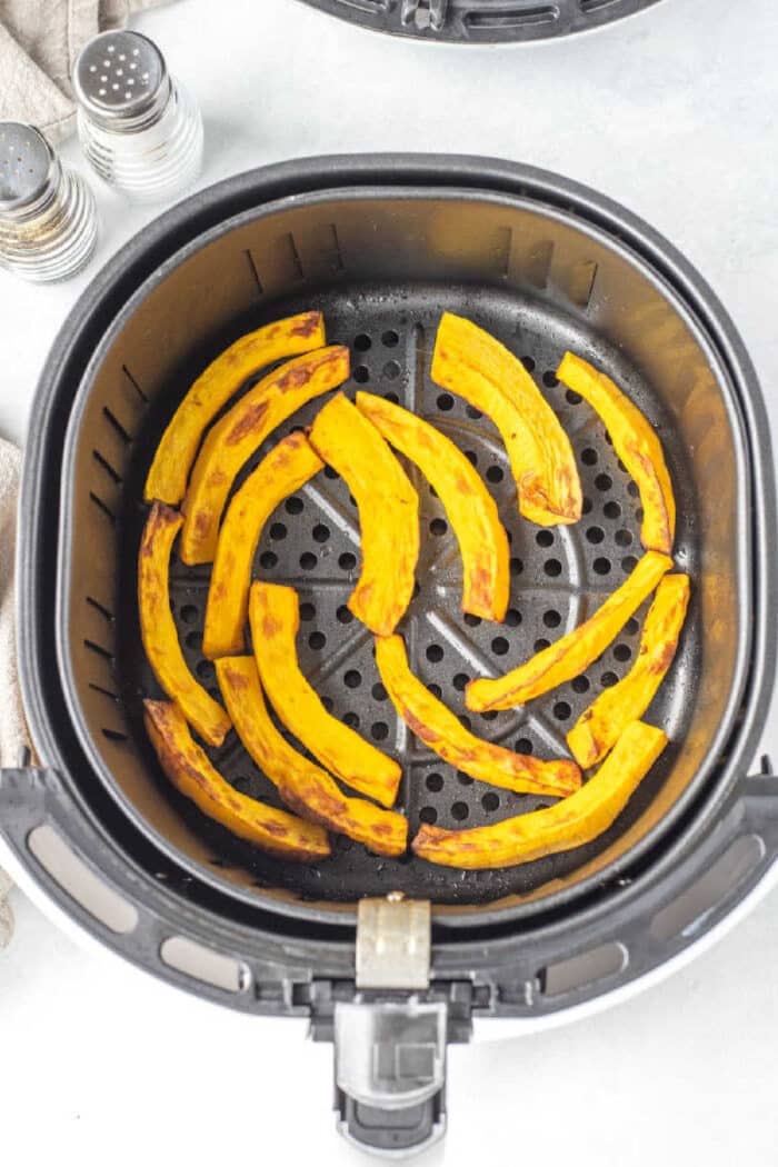 Curved slices of air fryer pumpkin in a basket, with salt and pepper shakers nearby.