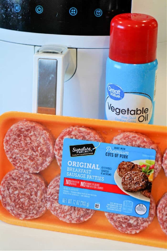 A tray of raw sausage patties and a can of vegetable oil sit next to an air fryer, ready for you to make delicious sausage patties in air fryer with ease.