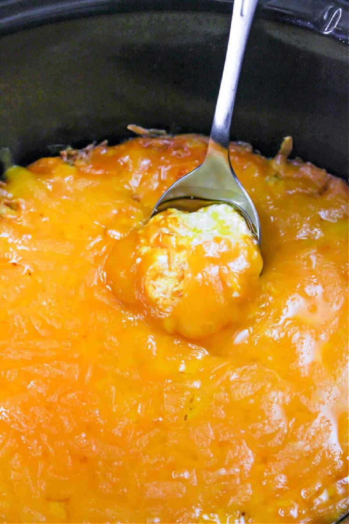 A spoon scoops cheesy, golden-brown Publix Buffalo Chicken Dip from a baking dish.