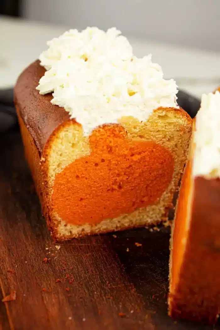 A sliced pound cake with a circular orange filling inside the cake. The top of this delightful shape cake is decorated with a generous layer of white frosting. The cake sits on a wooden cutting board.