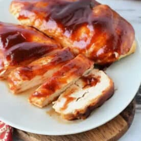 Air fryer BBQ chicken breast, sliced and coated in tangy barbecue sauce, served on a white plate atop a wooden board.