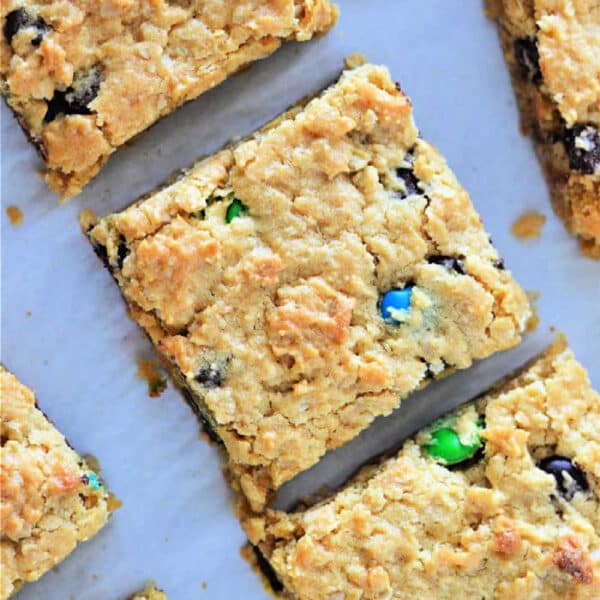 Golden cookie bars from cake mix studded with chocolate chips and colorful candy pieces, cut into squares on parchment paper.