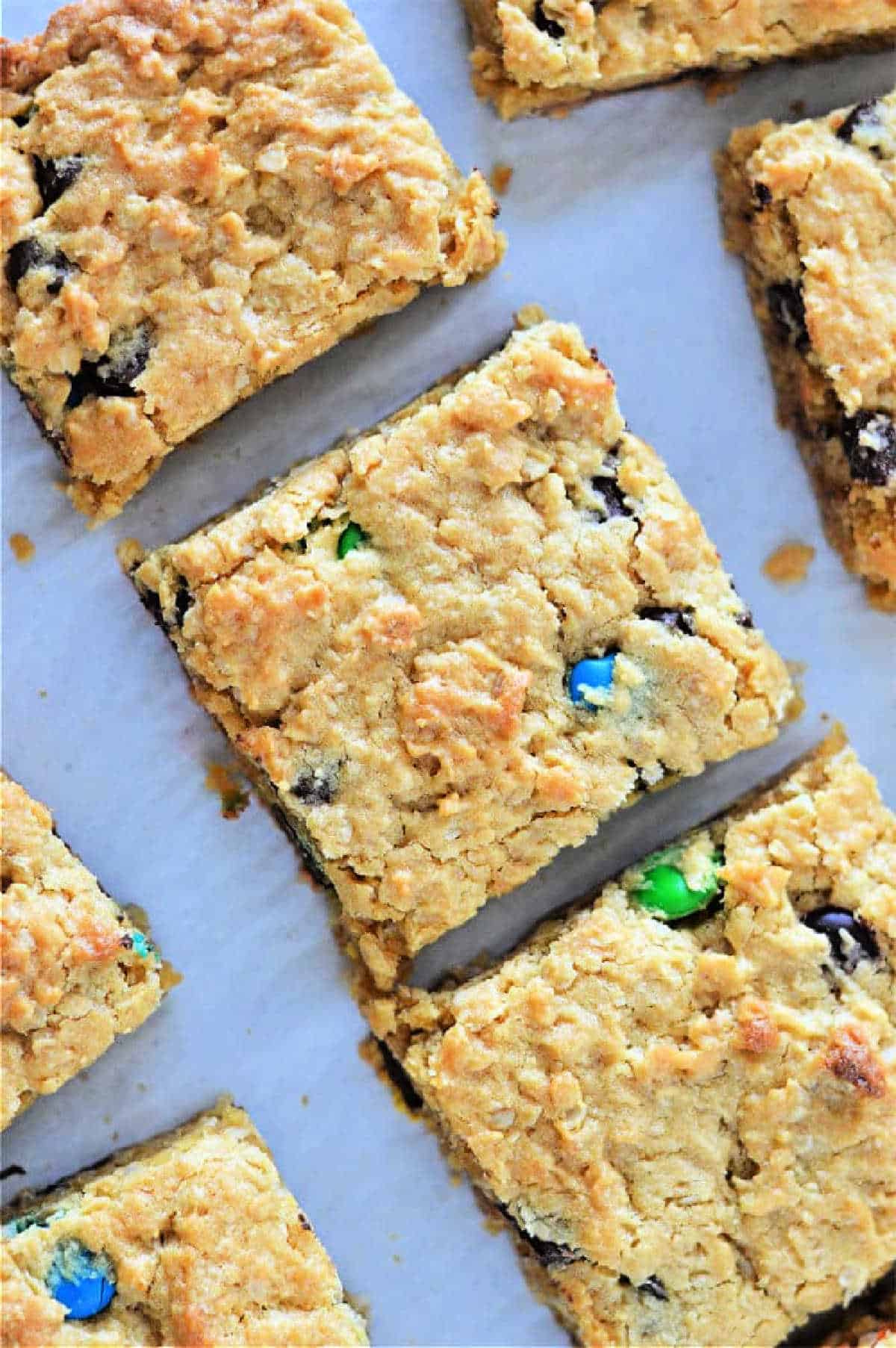 Golden cookie bars from cake mix studded with chocolate chips and colorful candy pieces, cut into squares on parchment paper.