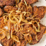 Fried beef liver pieces topped with caramelized onions on a white plate—a classic dish for those learning organ meats, just like when discovering how to cook beef heart.