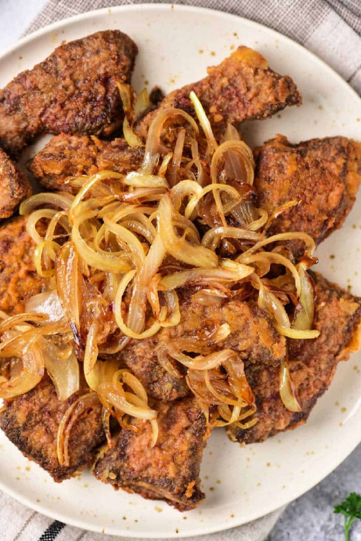 Fried bee heart pieces topped with caramelized onions on a white plate—a classic dish for those learning organ meats, just like when discovering how to cook beef heart.