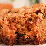 Close-up of a moist slice of chocolate chip cookie cake on a white plate, resembling the perfect blend achieved when learning how to make brookies with brownie mix and cookie dough. The golden-brown crust and melted chocolate chips create a deliciously textured and rich appearance.