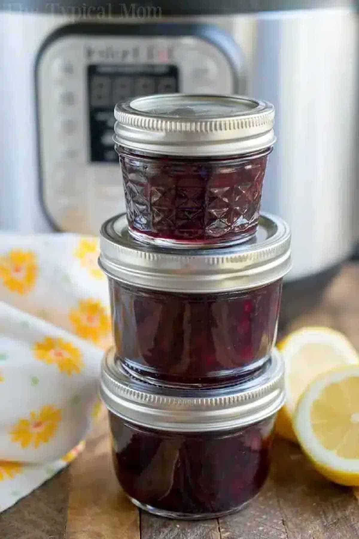 Pressure cooker jam takes 15 minutes and you can use any fruit. If you're wondering how to make Instant Pot homemade jam or in a Ninja Foodi. Here it is. #instantpot #pressurecooker #jam #jelly #strawberry #huckleberry #homemade #berry #instantpotrecipes #thetypicalmom #ninjafoodi Three small jars of homemade pressure cooker jam are stacked in front of an Instant Pot, with lemon slices beside them.