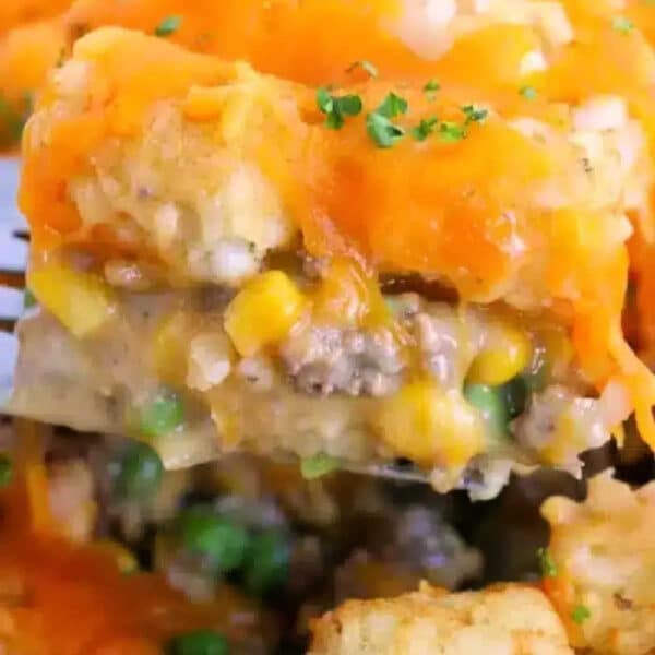 A close-up of a potato tot casserole with ground beef, corn, peas, and gooey melted cheddar cheese.