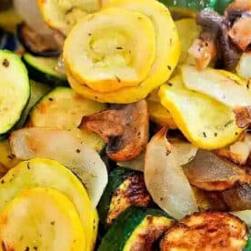 Saut&eacute;ed yellow squash, zucchini, onions, and mushrooms&mdash;delicious air fryer vegetables&mdash;served on a white plate with a purple border.