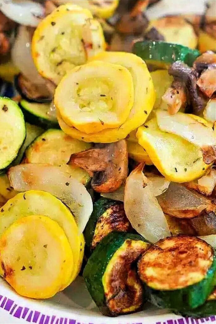 Saut&eacute;ed yellow squash, zucchini, onions, and mushrooms&mdash;delicious air fryer vegetables&mdash;served on a white plate with a purple border.