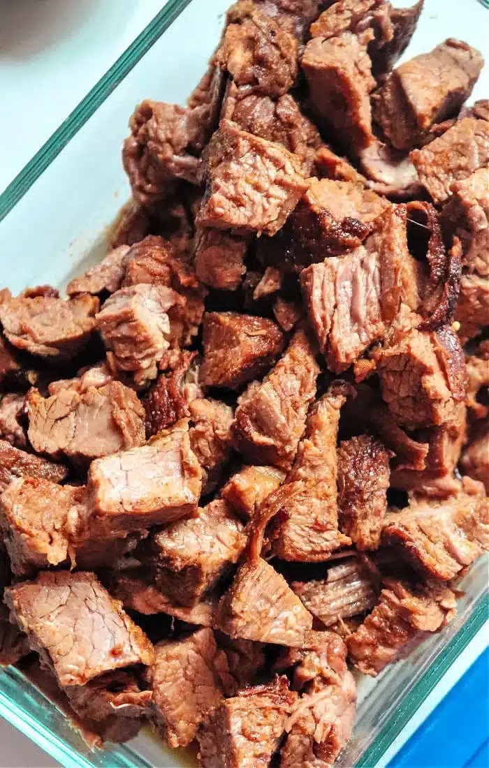 A clear glass container filled with many pieces of cooked, cubed beef brisket, likely prepared in an air fryer. The meat appears browned and slightly crispy on some edges.