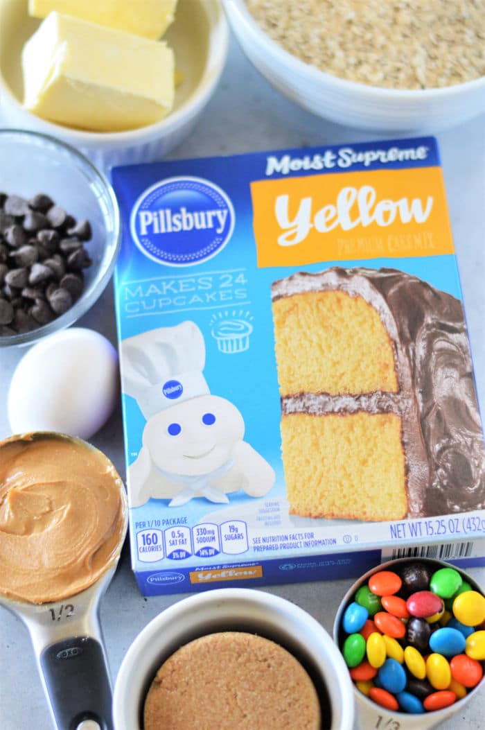 Box of Pillsbury yellow cake mix surrounded by butter, chocolate chips, egg, peanut butter, and candy&mdash;perfect for making delicious Cookie Bars From Cake Mix.