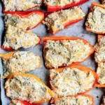 A baking sheet lined with parchment paper holds several halved, Stuffed Mini Sweet Peppers brimming with a creamy, herb-filled mixture. The text "Stuffed Mini Peppers!" is prominently displayed at the top.