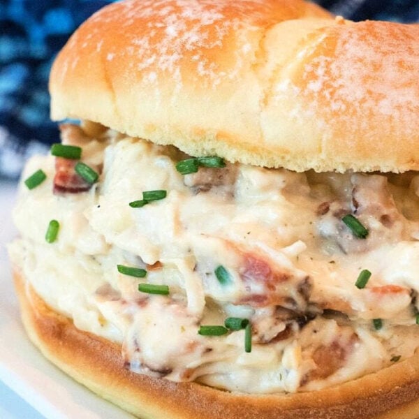Creamy crockpot crack chicken and bacon sandwich with chopped chives on a bun, served on a white plate.
