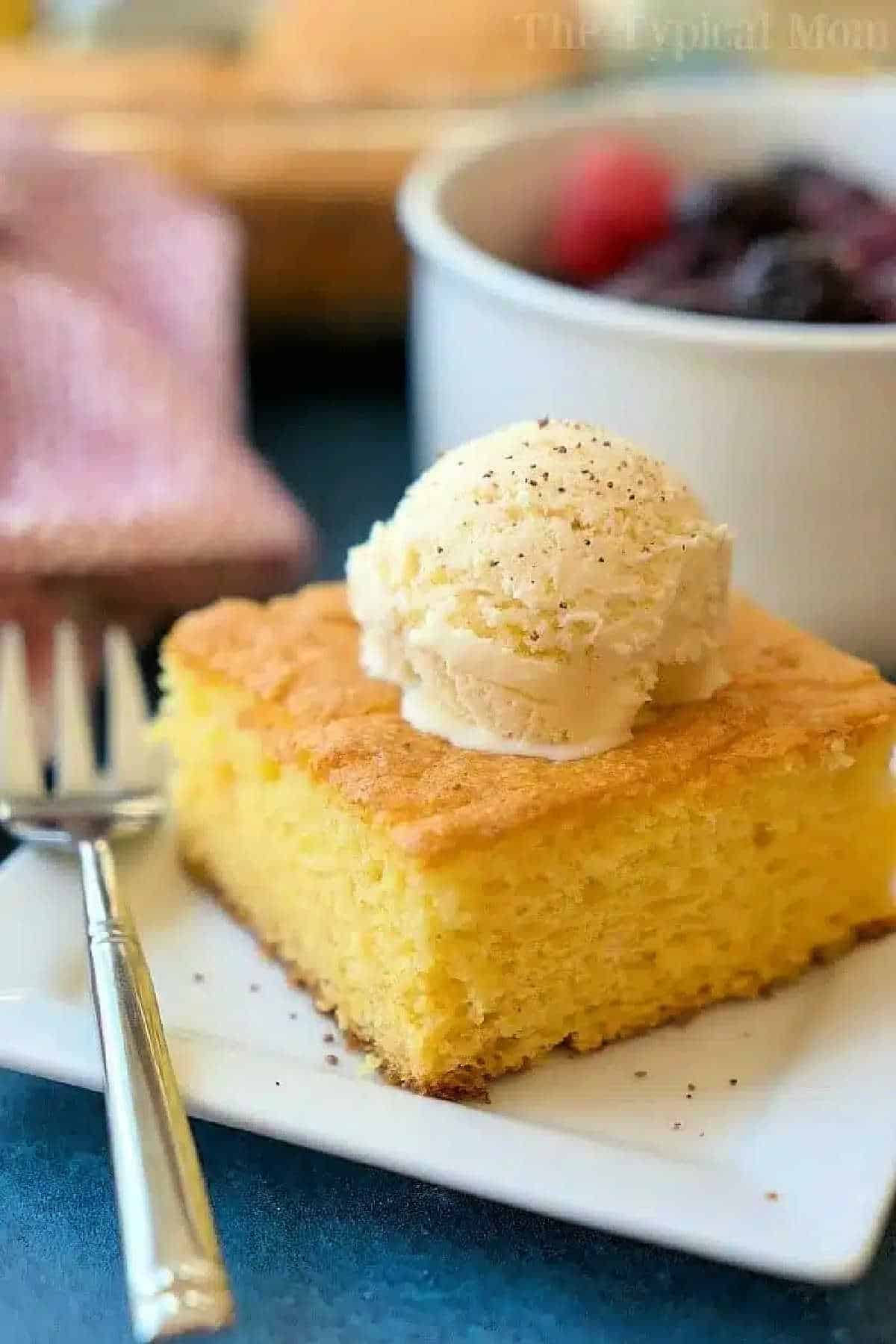 A slice of egg nog pudding cake topped with vanilla ice cream on a white plate with a fork beside it.