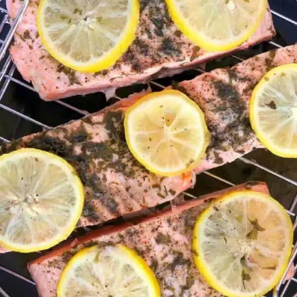 Three salmon fillets topped with lemon slices and herbs on a metal rack, perfect for making instant pot frozen salmon.