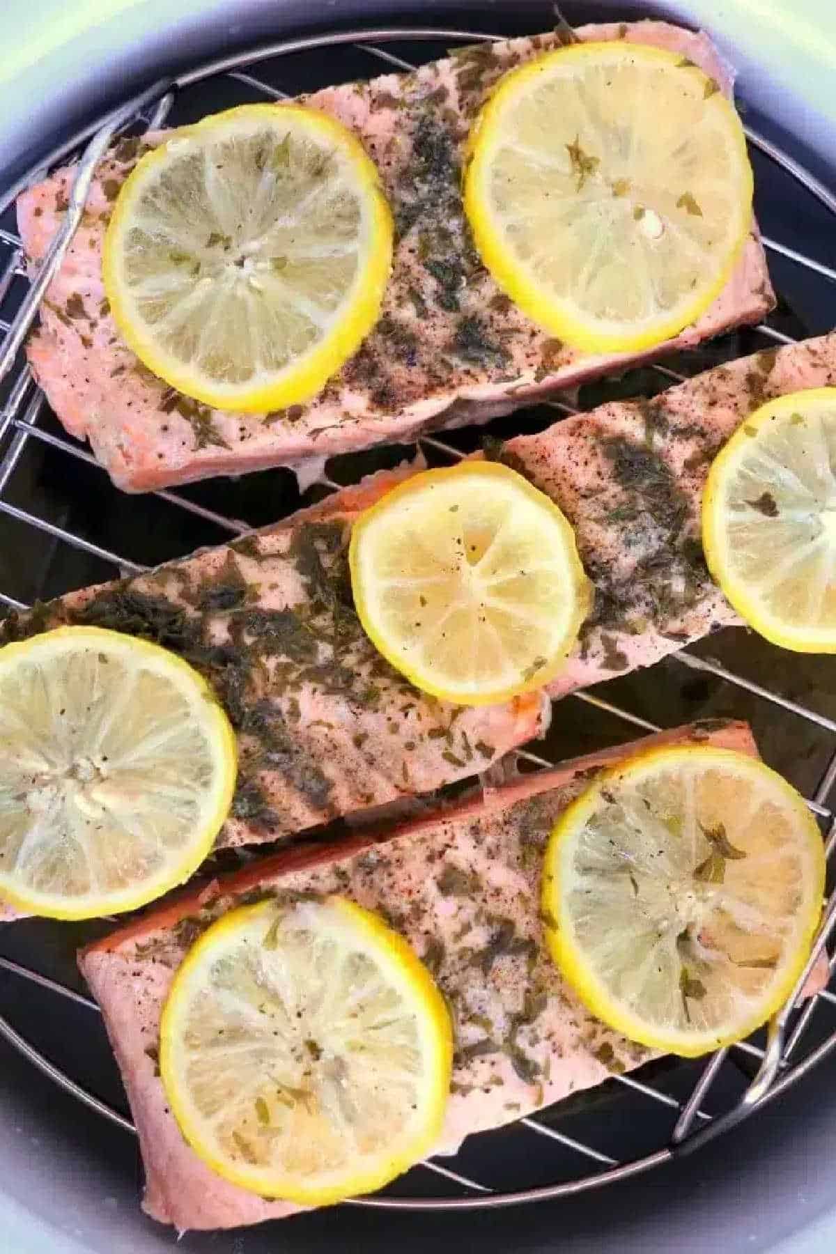 Three salmon fillets topped with lemon slices and herbs on a metal rack, perfect for making instant pot frozen salmon.