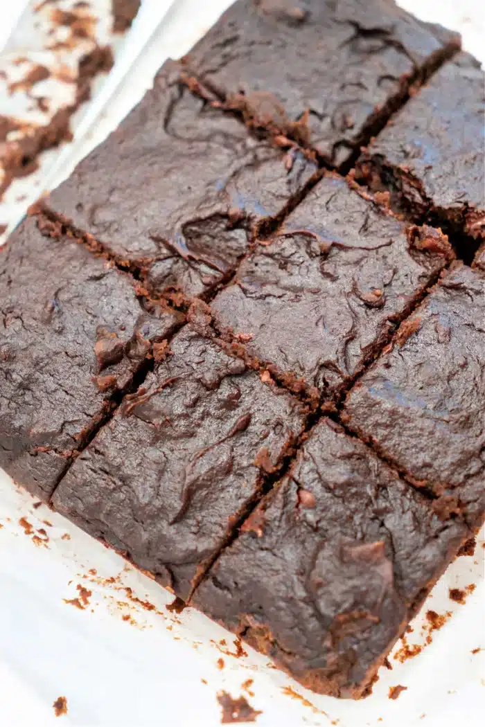 A close-up view of a batch of pumpkin brownies cut into squares reveals their rich, dense texture with a delightful chocolatey appearance. Visible at the edges are some crumbs and chunks of chocolate pieces, adding to their tempting allure.