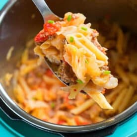 A spoonful of pasta with ground meat and vegetables, reminiscent of a hearty pressure cooker sausage and cabbage dish, held above a pot of pasta.