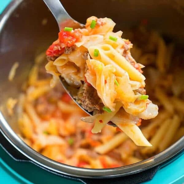A spoonful of pasta with ground meat and vegetables, reminiscent of a hearty pressure cooker sausage and cabbage dish, held above a pot of pasta.