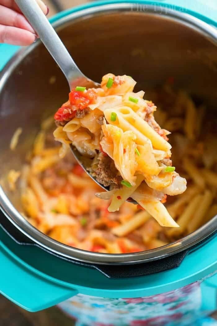 A spoonful of pasta with ground meat and vegetables, reminiscent of a hearty pressure cooker sausage and cabbage dish, held above a pot of pasta.
