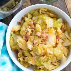 Bowl of pressure cooker fried cabbage with bacon pieces, next to a small bowl of chopped chives on a wooden table.