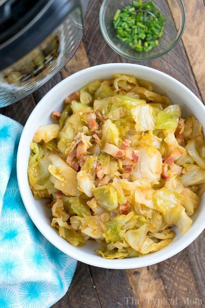 Instant Pot fried cabbage is amazing! If you love cabbage and bacon you will enjoy this. Love my Instant Pot! #instantpot #instantpotrecipes #pressurecooker #bacon #friedcabbage #cabbage #thetypicalmom Bowl of pressure cooker fried cabbage with bacon pieces, next to a small bowl of chopped chives on a wooden table.