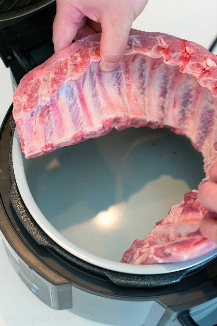 Hands placing a rack of raw ribs into an open pressure cooker, preparing delicious Ninja Foodi ribs.