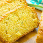 Close-up of sliced zucchini pineapple bread on a wooden surface, with a blue floral towel in the background.