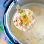 A ladle of creamy Instant Pot cheeseburger soup with cheese, ground meat, and chives is held over an Instant Pot.