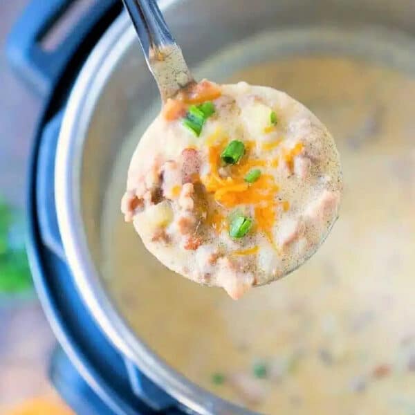 A ladle of creamy Instant Pot cheeseburger soup with cheese, ground meat, and chives is held over an Instant Pot.