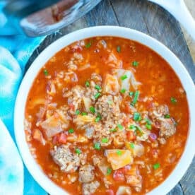 A bowl of hearty pressure cooker cabbage soup with ground beef, rice, and tomatoes sits on a wooden table.