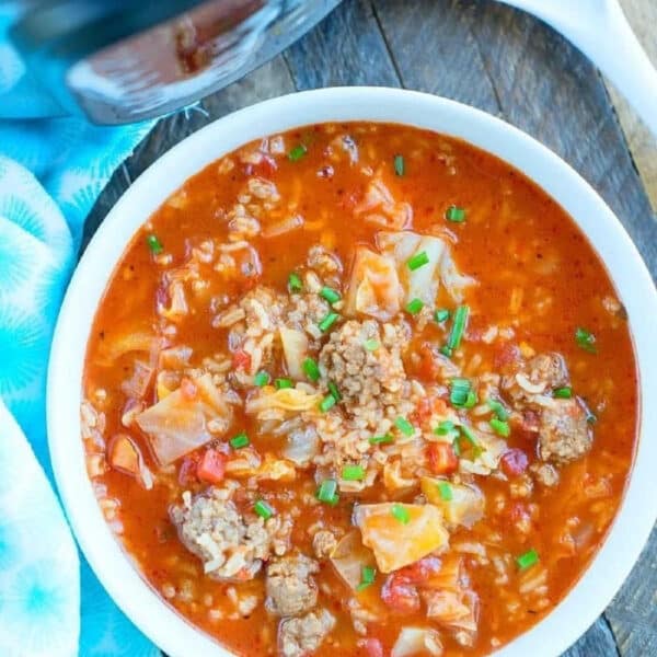 A bowl of hearty pressure cooker cabbage soup with ground beef, rice, and tomatoes sits on a wooden table.