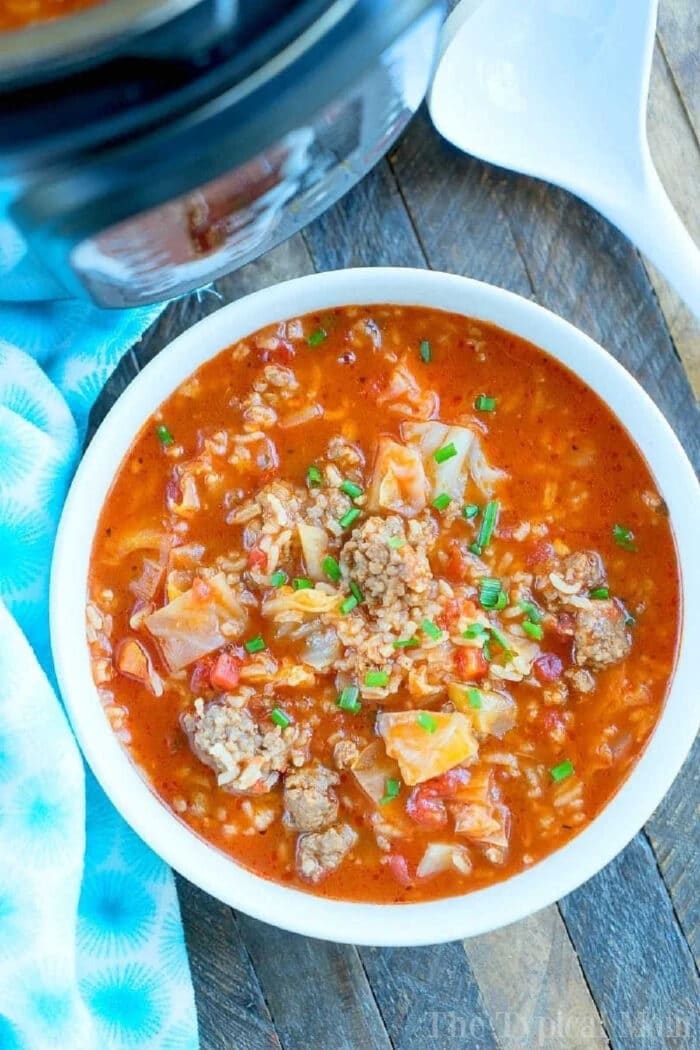 Instant Pot cabbage soup recipe! If you love your Instant Pot and cabbage then this may become your favorite dinner ever! #instantpot #pressurecooker #cabbage #soup #thetypicalmom #groundbeef #sausage #instantpotrecipes A bowl of hearty pressure cooker cabbage soup with ground beef, rice, and tomatoes sits on a wooden table.
