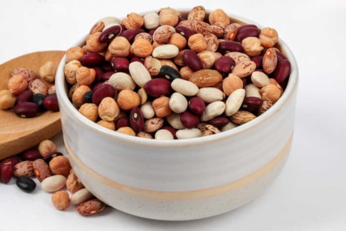 A white bowl filled with assorted dried beans, perfect for making pressure cooker chili with dry beans, with more beans scattered in a wooden dish nearby.