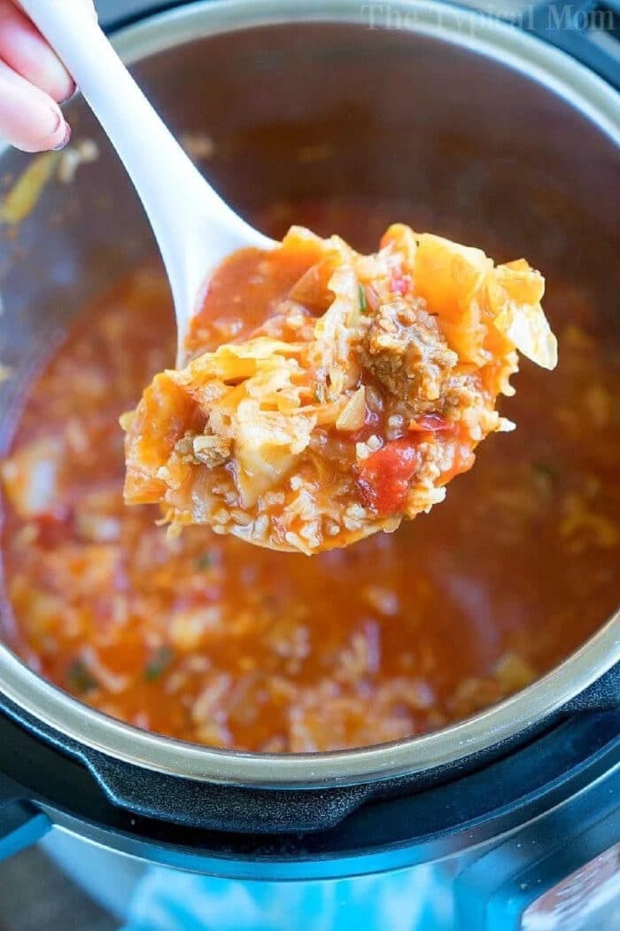 Pressure cooker cabbage soup recipe! If you love your Instant Pot and cabbage then this may become your favorite dinner ever! #instantpot #pressurecooker #cabbage #soup #thetypicalmom #groundbeef #sausage #instantpotrecipes A ladle of hearty pressure cooker cabbage soup with ground meat and tomatoes held over a pot.
