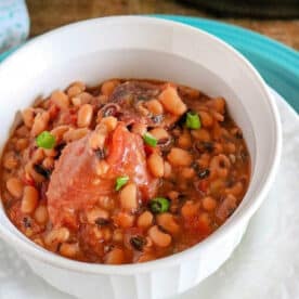 A white bowl filled with pressure cooker black eyed peas and ham in broth, garnished with green onions.