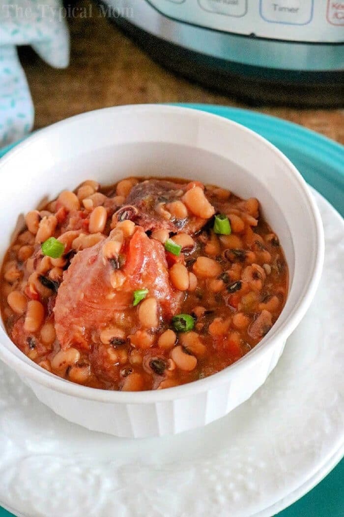 A white bowl filled with pressure cooker black eyed peas and ham in broth, garnished with green onions.