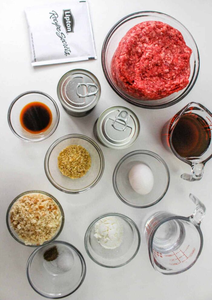 Top view of raw ground beef, seasonings, sauces, egg, breadcrumbs, and canned soup ingredients on a white surface&mdash;perfect for making a classic Chopped Steak Recipe.