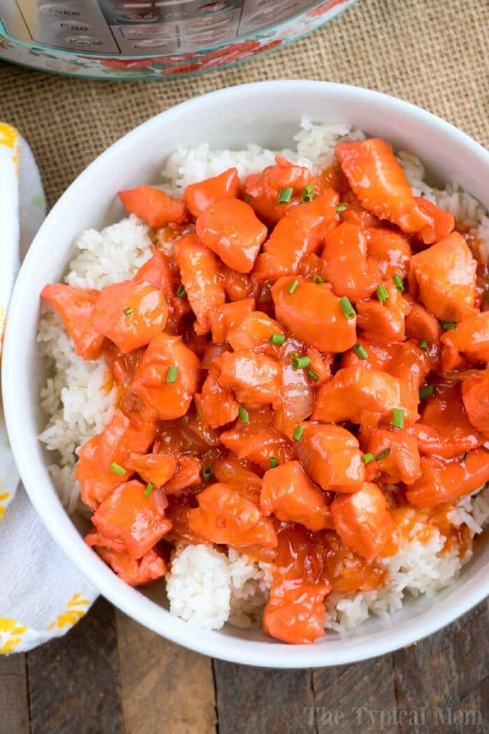 Pressure Cooker apricot chicken just needs 5 ingredients and is the perfect dinner atop a bed of rice! If you have an Instant Pot you've gotta' try this! #instantpotrecipes #instantpot #apricotchicken #chicken #dinner #pressurecooker #ninjafoodi #thetypicalmom Bowl of white rice topped with pressure cooker apricot chicken, garnished with chopped green onions.