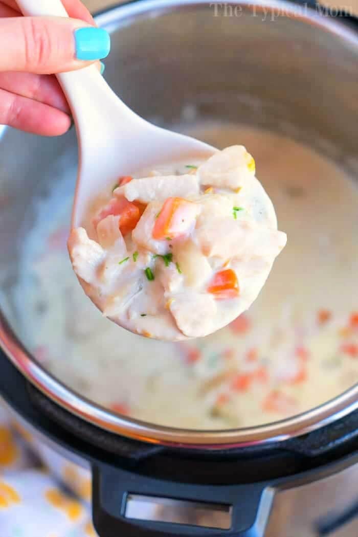 A spoonful of creamy chicken pot pie soup with vegetables held over an Instant Pot.