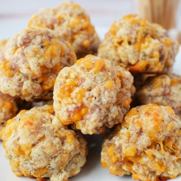 A plate of baked sausage balls with cheese, crafted from biscuit mix, piled together on a white dish.