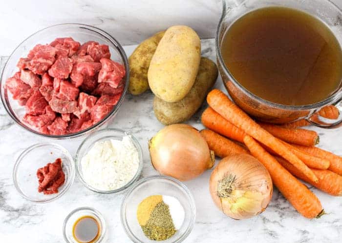 Raw beef, potatoes, carrots, onions, broth, flour, tomato paste, spices, and sauce on a marble surface&mdash;perfect for making Slow Cooker Beef Stew with Onion Soup Mix.