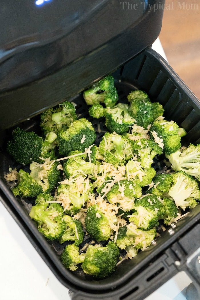 Fresh broccoli florets with shredded cheese sit in an air fryer basket, perfect for making delicious broccoli in air fryer.