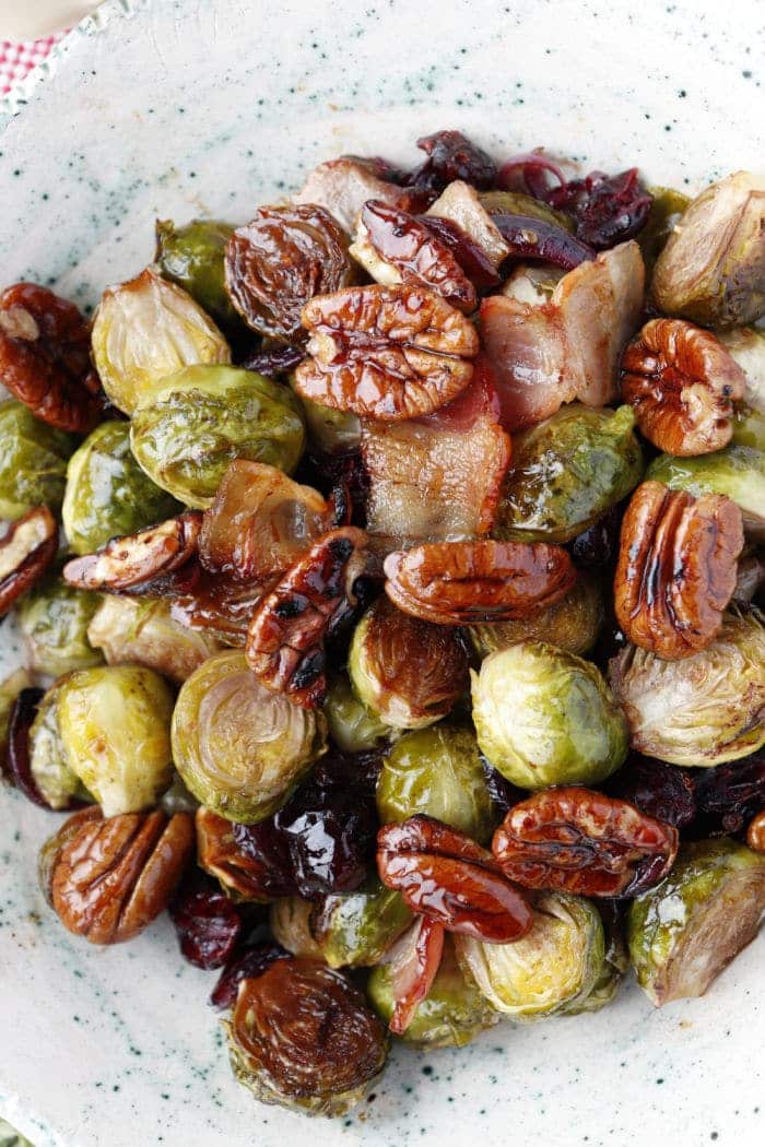 Roasted frozen brussel sprouts air fryer style with pecans, bacon, and cranberries on a white speckled plate.