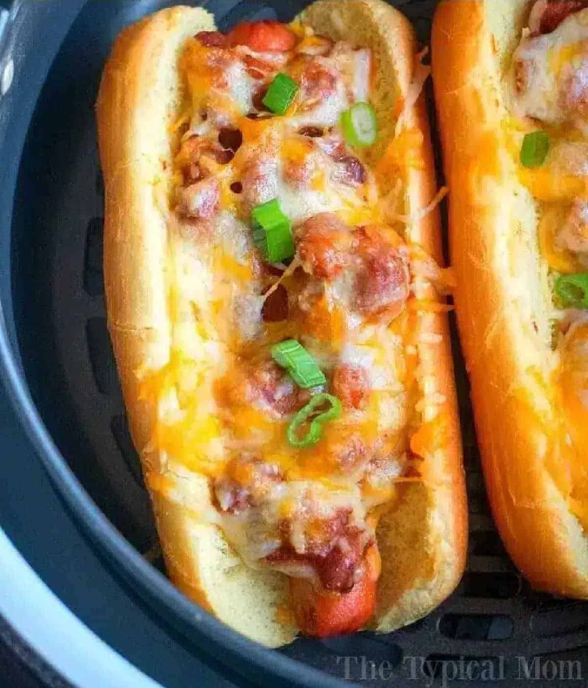 An air fryer hot dog topped with chili, melted cheese, and chopped green onions in a toasted bun.