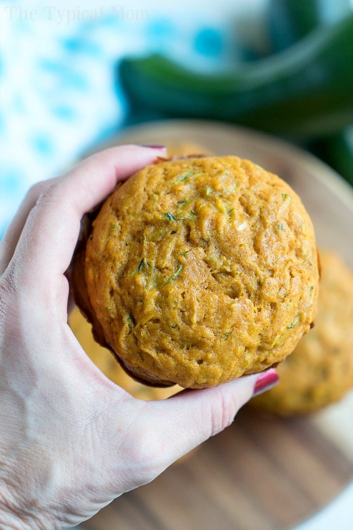 A hand holding a round, golden brown zucchini muffin with a soft texture&mdash;an easy muffin recipe perfect for delicious homemade treats.