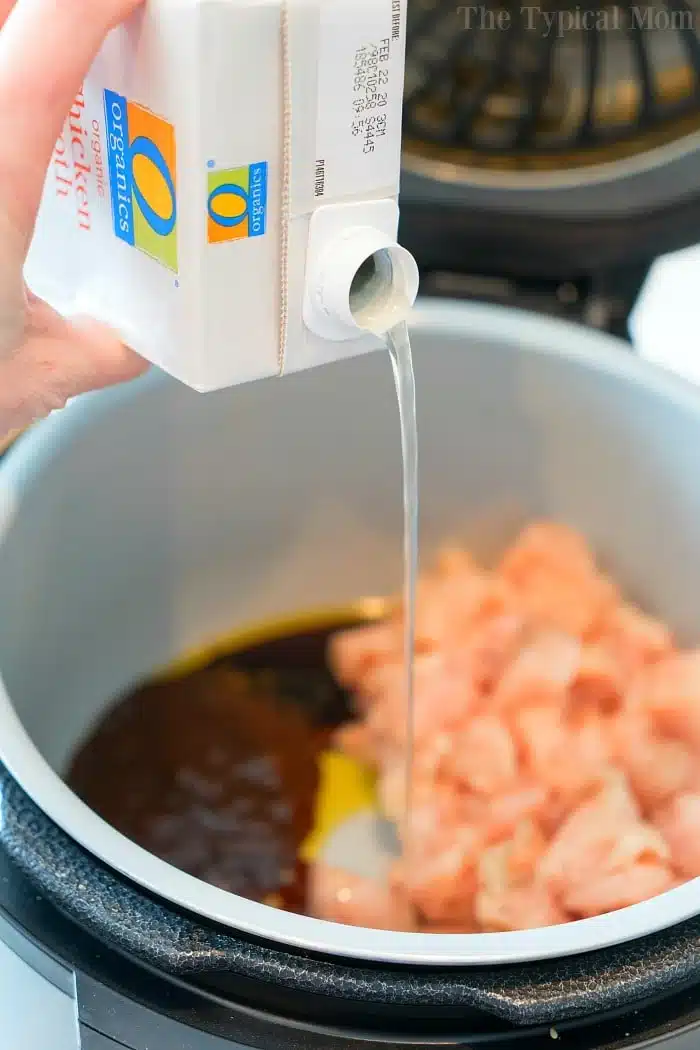 Broth is being poured from a carton into a pressure cooker cashew chicken dish with diced chicken and sauce inside.