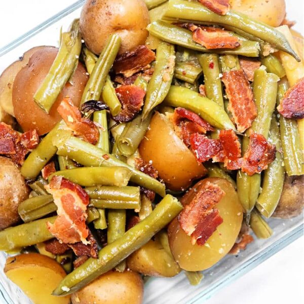 Green Beans with Ham and Potatoes are served together in a clear glass dish, showcasing green beans, small potatoes, and savory bacon pieces on a white background.